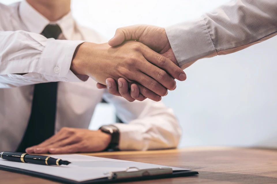 Deux hommes d'affaires en chemise blanche se serrent la main au-dessus d'un bureau, finalisant visiblement un accord commercial